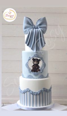 a three tiered cake with a teddy bear on top and blue ribbon around the edge