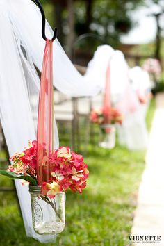 flowers in mason jars are hanging from the back of an outdoor wedding ceremony set up