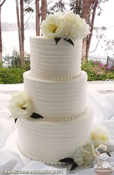 a wedding cake with white flowers on top is sitting in the middle of a table