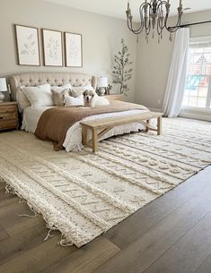 a bedroom with a large bed, chandelier and two windows in the background