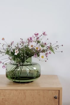 a glass vase with flowers in it sitting on a wooden table next to a white wall