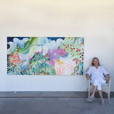 a woman sitting on a chair in front of a large painting hanging on the wall