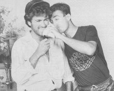 black and white photograph of two men sitting next to each other, one holding something in his mouth