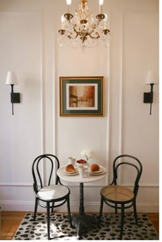 two chairs and a table with food on it in front of a chandelier