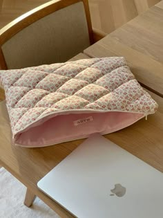 an apple laptop computer sitting on top of a wooden table next to a pink pillow