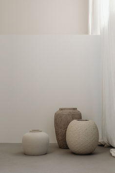 two white vases sitting next to each other on the floor in front of a window