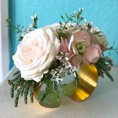 a gold vase with white and pink flowers in it sitting on a table next to a blue wall