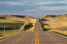 an empty road with no cars on it in the middle of some grass covered hills