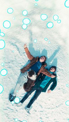 two people are laying in the snow with their arms around each other and one person is holding a dog