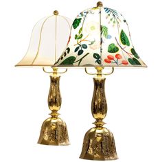 two golden lamps with floral designs on them, one has a white shade and the other is gold