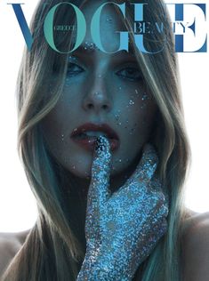 a woman with blue glitter on her face and hand over her mouth, posing for the cover of a magazine