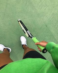 a person holding a tennis racquet on top of a green court with white shoes