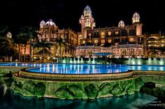 a large building lit up at night next to a fountain with lights in the water