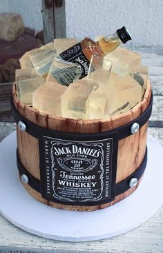 a wooden barrel cake with ice cubes and whiskey bottles on top, sitting on a white plate