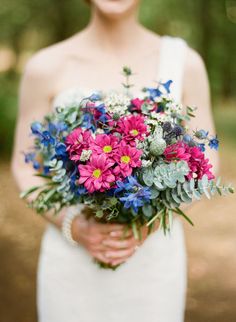 a woman in a white dress holding a bouquet of pink, blue and green flowers