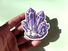 a hand holding a purple sticker with crystals on it's back and in the middle