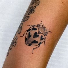 a ladybug tattoo on the arm with black dots and hearts in its center