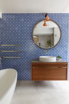 a bathroom with blue and white tiles on the walls, a round mirror above the sink