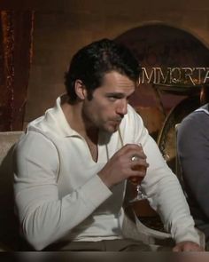 two men sitting next to each other drinking wine