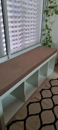 a white bench sitting in front of a window next to a rug and potted plant