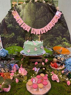 a birthday cake and cupcakes on a table with flowers, greenery and decorations