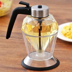 a glass tea pot with a black handle on a table next to macaroni and cheese