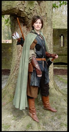 a woman dressed in medieval clothing standing next to a tree with an arrow on it