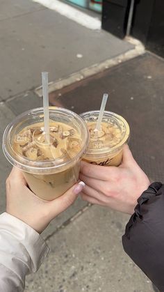 two people are holding drinks with straws in their hands on the sidewalk near a building