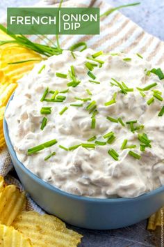 a blue bowl filled with white dip surrounded by green onions and chips on a napkin