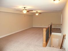 an empty living room with ceiling fans and carpeted stairs leading up to the second floor