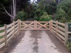 a wooden gate is open on the side of a dirt road with trees in the background