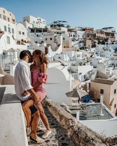 a man and woman sitting on top of a building next to each other with buildings in the background