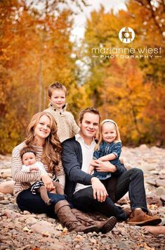 a family sitting on rocks in the woods with fall foliage around them and trees behind them