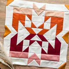 an orange and white quilt on top of a wooden table next to a feather ornament