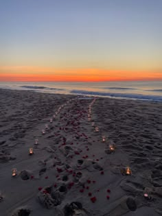 candles are lined up in the sand on the beach as the sun sets over the ocean