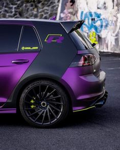 a purple car parked in front of a wall with graffiti on it's side