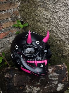 a black helmet with pink spikes on it sitting in front of a tree trunk and stone wall