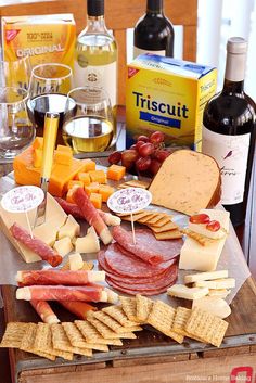 an assortment of cheeses, meats, and wine on a table with bottles of wine