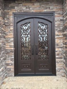 two brown doors with intricate iron work on the side of a brick building in front of a stone wall