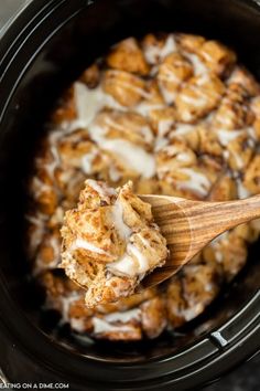 a wooden spoon in a slow cooker filled with cinnamon rolls and cream cheese sauce