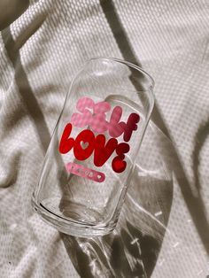 a clear glass with red and pink stickers on it sitting on a white sheet