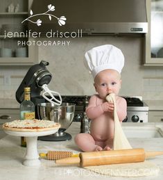 a baby is sitting on the kitchen counter with a pizza and rolling pan in front of him