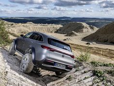 a silver car driving on top of a dirt hill next to trees and grass covered hills