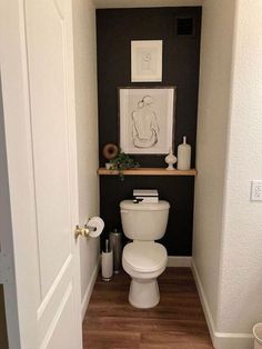 a white toilet sitting inside of a bathroom next to a wooden floor and framed artwork