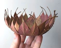 a hand holding up a paper crown with leaves on it's sides and gold flecks around the edges