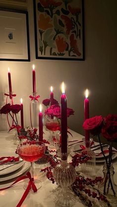 the table is set with candles, plates and red roses in glass vases on it