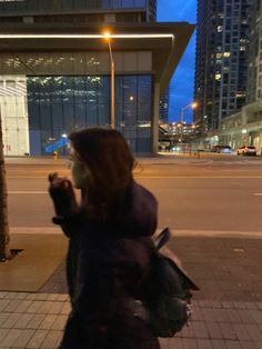 a woman is walking down the street at night with her cell phone in her hand