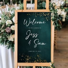 a welcome sign with greenery and white flowers on the table at a wedding reception