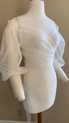 a mannequin wearing a white dress with ruffles on the sleeves and shoulders