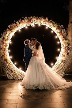 a bride and groom standing in front of a wedding arch with fairy lights on it